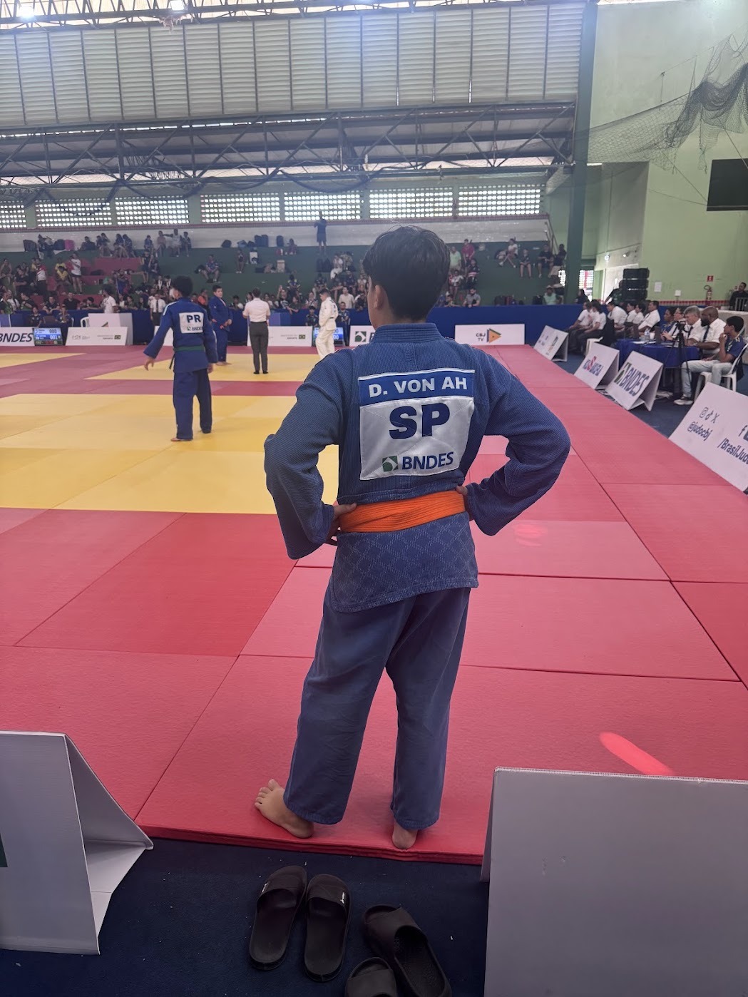 Davi Von Ah de judogi azul com o dorsal SP, observando as lutas no tatame do Ginásio Poliesportivo do IFAP