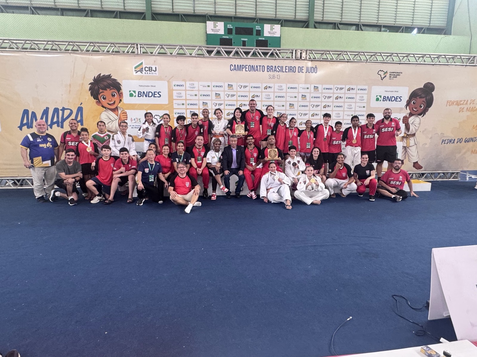 Medalhistas e senseis da delegação paulista reunidos diante do painel do Campeonato Brasileiro de Judô Sub-13