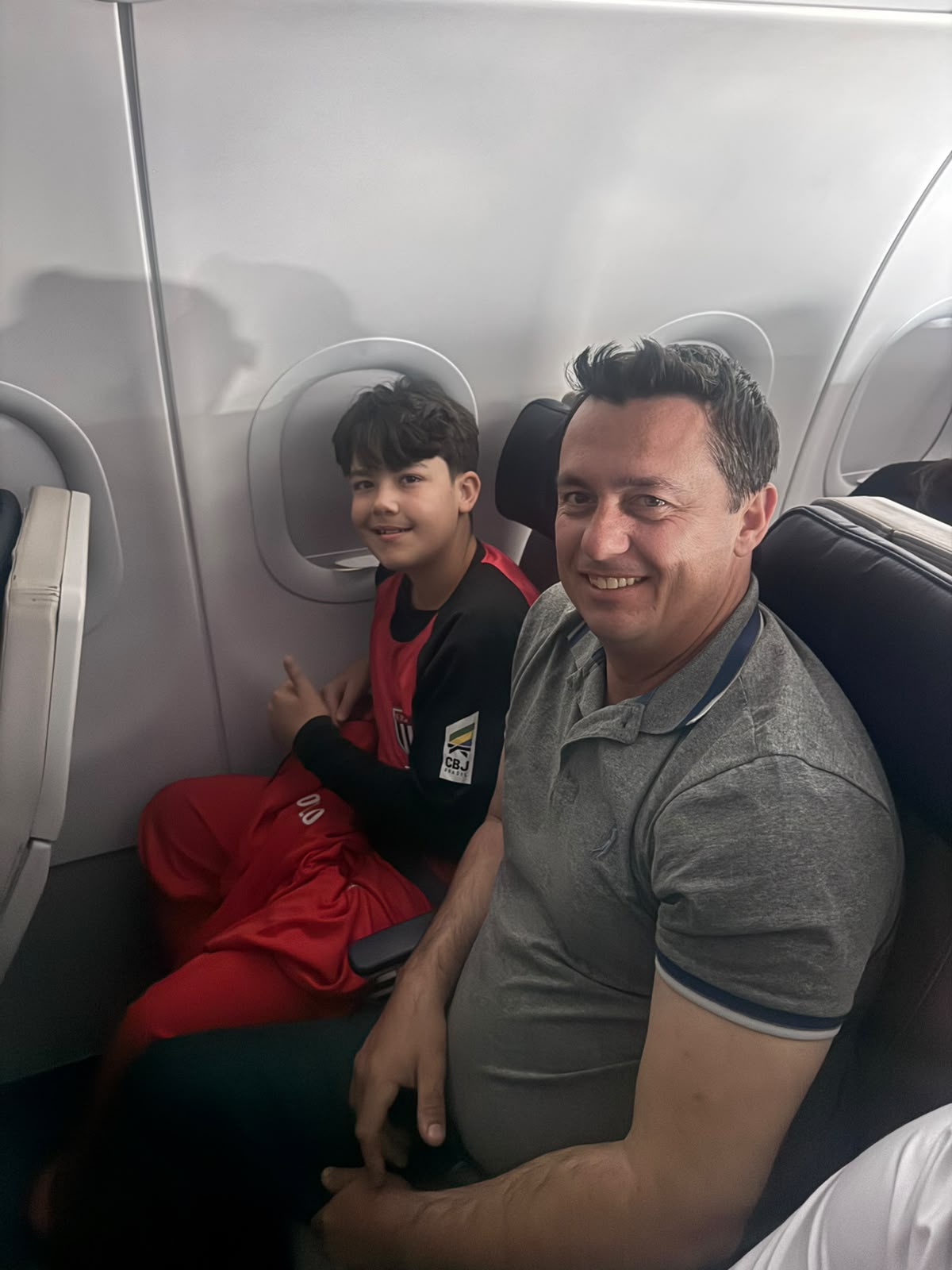 Atleta do Judô Honda a bordo do avião, sentado na janela com a camisa da seleção paulista, ao lado de um acompanhante