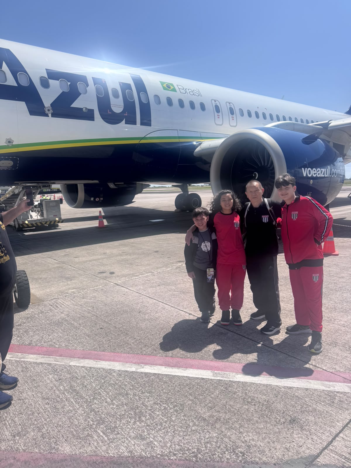 Lídia, Sensei Sergio Honda e Davi Von Ah abraçados na pista, em frente ao avião