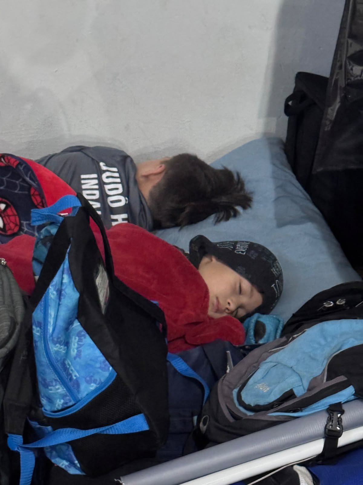 Samuel e Diego dormindo embrulhados em cobertores na arquibancada, em dia frio de campeonato
