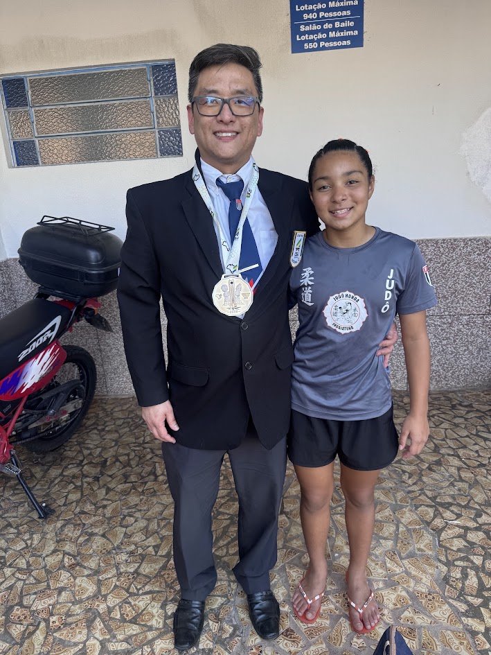 Sensei Fabiano de terno com a medalha de campeã brasileira no peito, ao lado da Lídia Sayuri