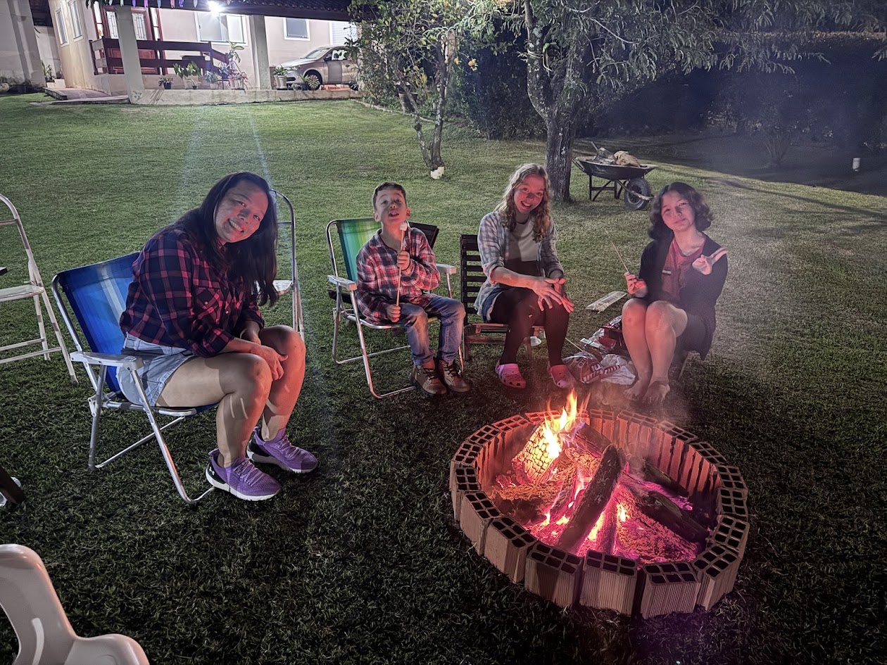 Fogueira acesa à noite na festa julina do Judô Honda, com integrantes da família Honda sentados ao redor