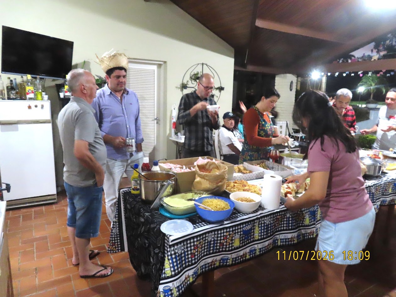 Mesa farta da festa julina do Judô Honda com pratos, panelas, molhos, comidas típicas em toalha xadrez