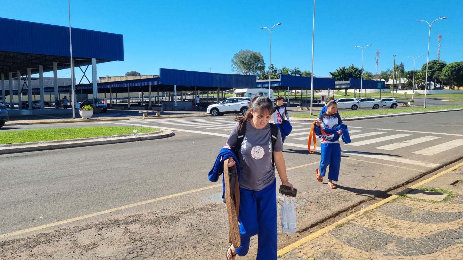 Fabiana Akemi e atletas da delegação Honda caminhando de judogi azul do alojamento para o Ginásio Domingão em Aguaí