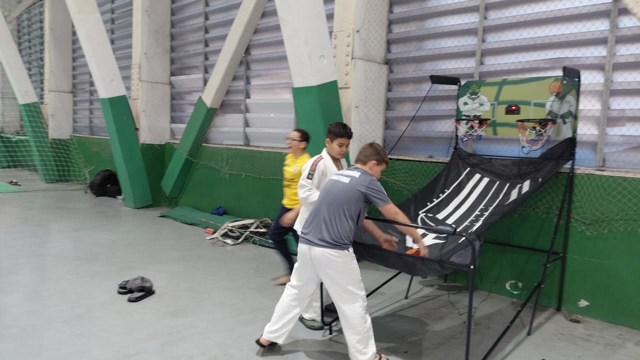 Atletas do Judô Honda se divertindo em um jogo de basquete de arcade no ginásio, entre as lutas do Torneio Periquito
