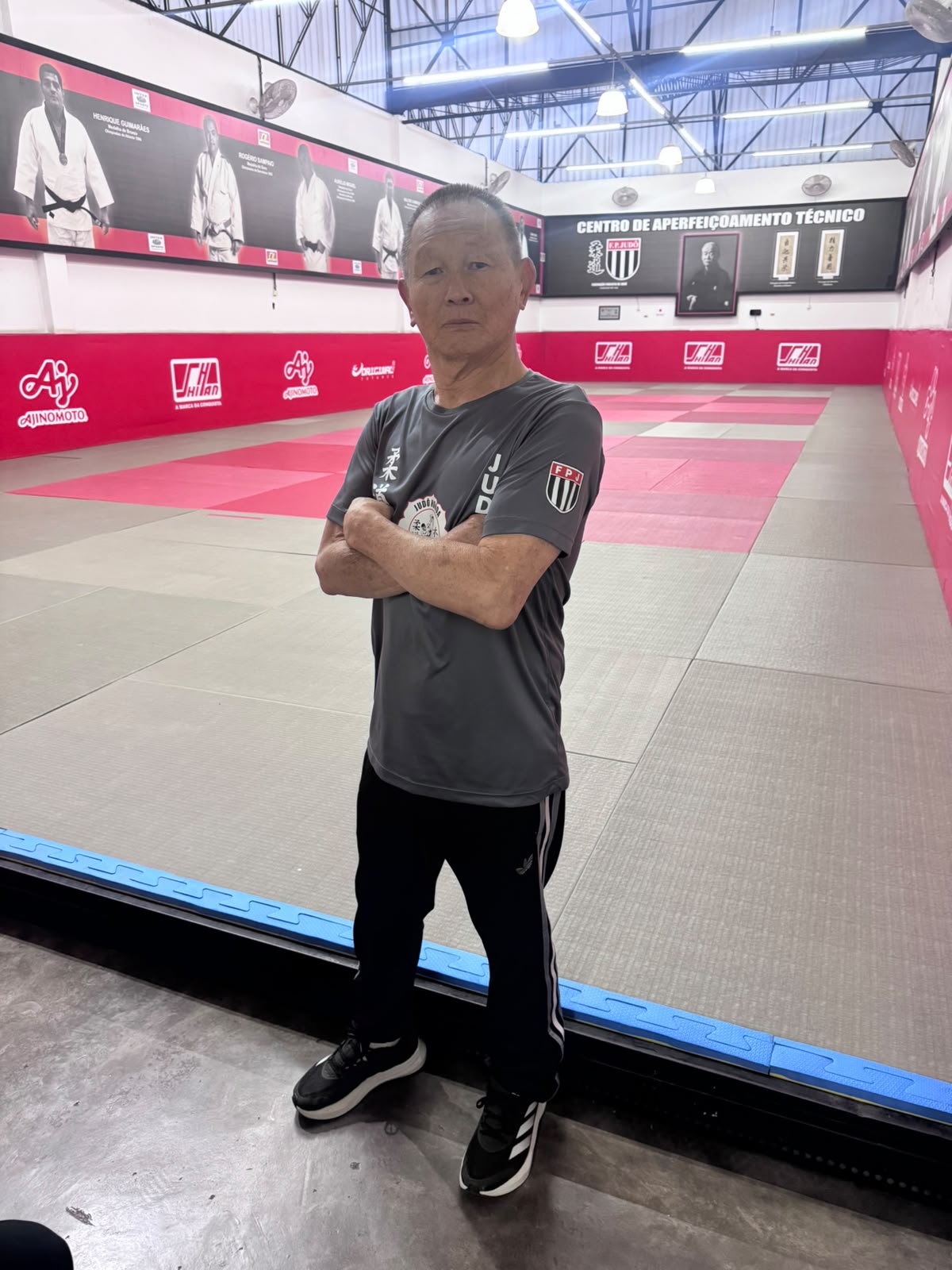 Sensei Sergio Honda de braços cruzados diante do tatame do Centro de Aperfeiçoamento Técnico, com os painéis dos medalhistas olímpicos paulistas ao fundo